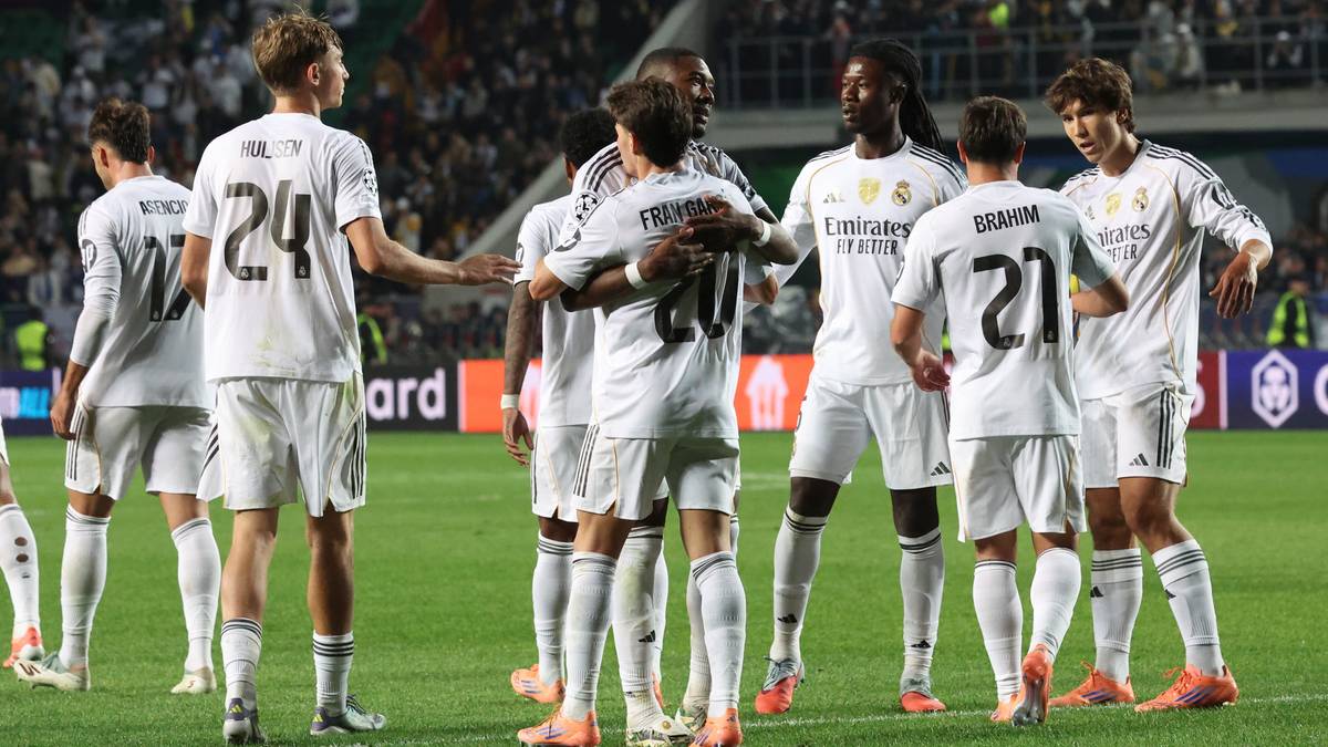 Drużyna piłkarska w białych strojach, z numerami na plecach, tworzy krąg na boisku.