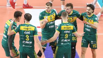 Siatkarze w zielonych strojach z żółtymi elementami, rozmawiający ze sobą na boisku.