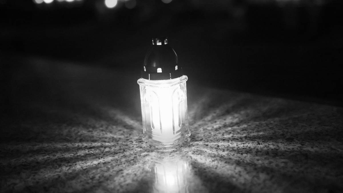 Pochylona na kamiennym blacie, jasno świecąca znicz z białym płomieniem.