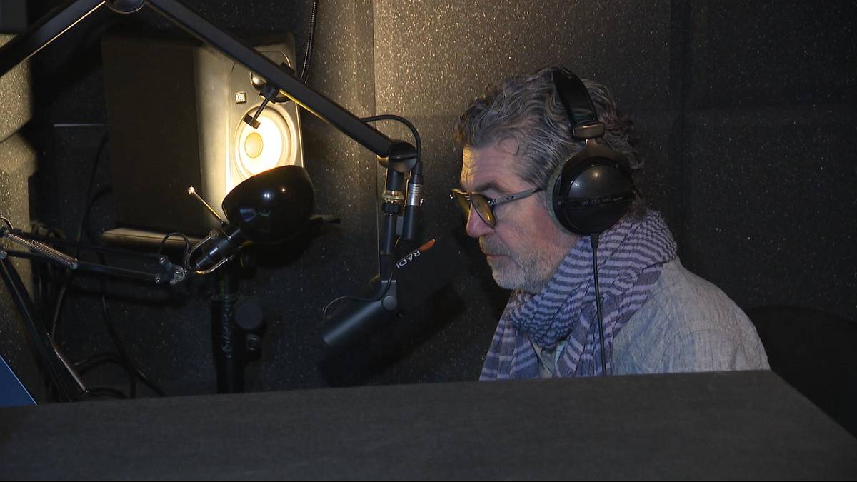 Lektor Jarosław Łukomski w słuchawkach przy mikrofonie w studiu nagraniowym.