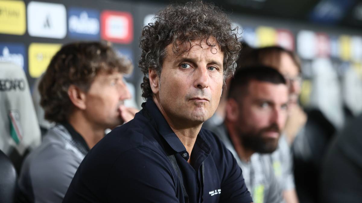 Portret z bliska mężczyzny z kręconymi włosami, ubranego w ciemną koszulkę polo.