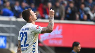 Piłkarz w białej koszulce z numerem 22 podnosi palec do g&oacute;ry, świętując bramkę.