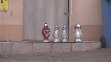 Cztery znicze stojące przed drzwiami kamienicy.