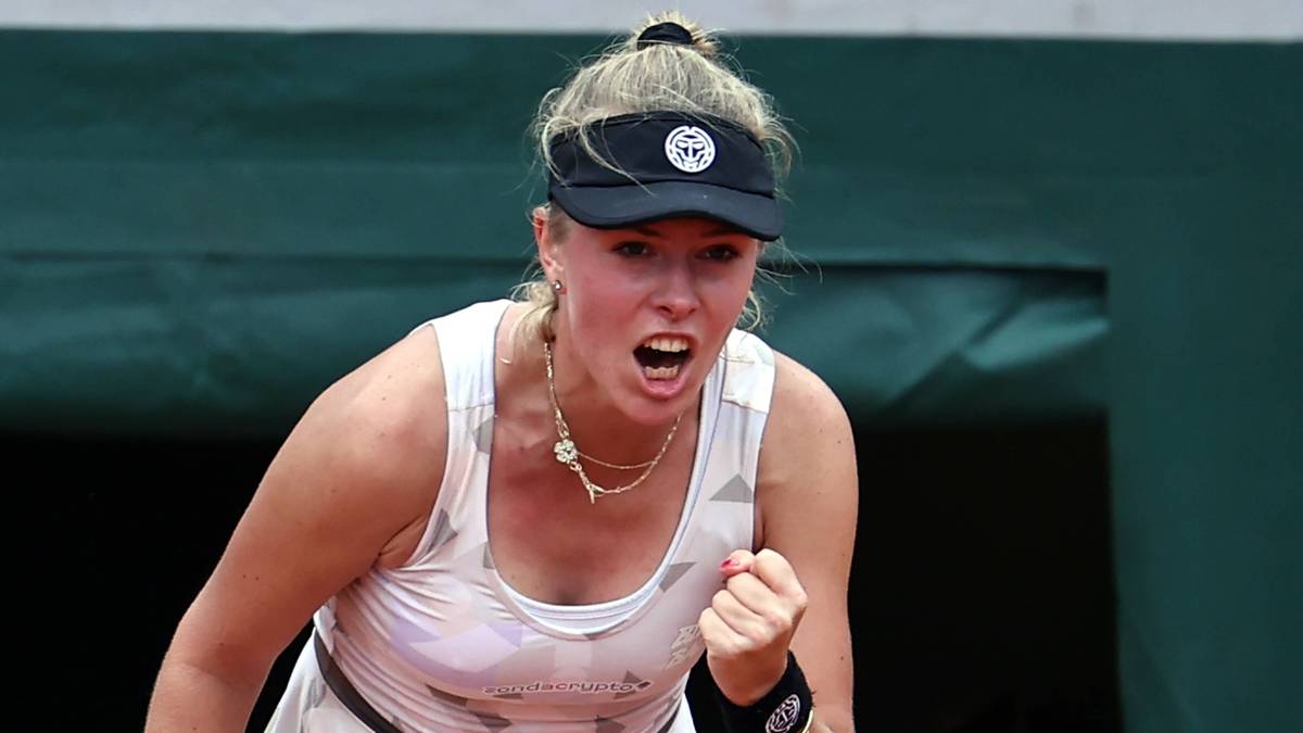 Tenisistka Magdalena Fręch w białej koszulce i czapce z daszkiem podczas meczu, z zaciętą miną i zaciśniętą pięścią.