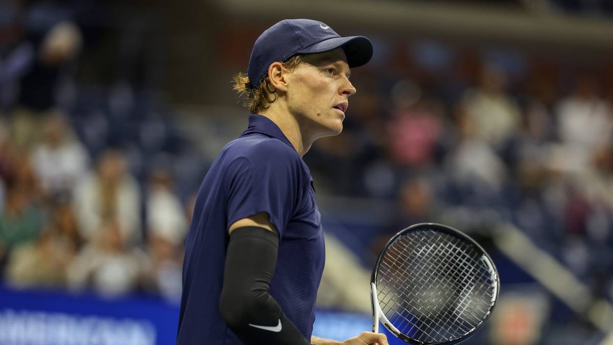 Mężczyzna w granatowej czapce i koszulce tenisowej z rakietą w ręku, grający w tenisa na korcie.