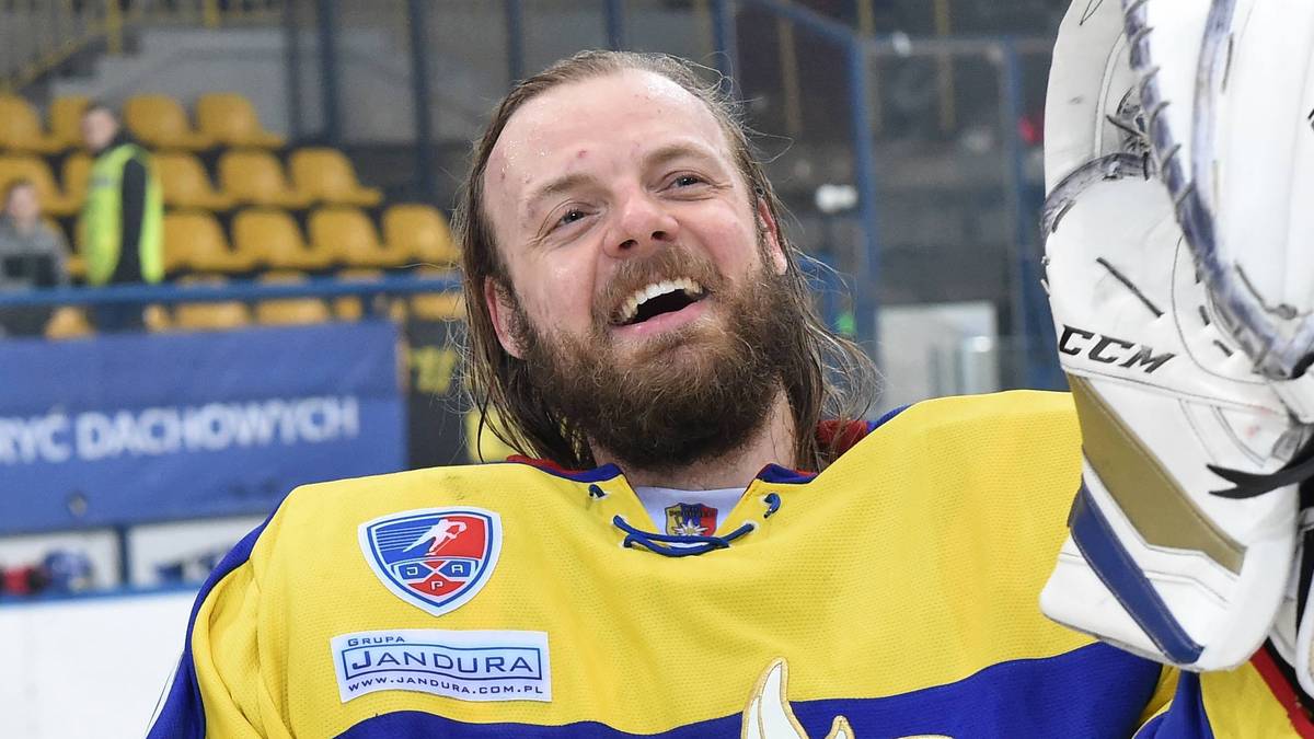 Hokeista w ż&oacute;łto-niebieskim stroju z rękawicą bramkarską w ręce, uśmiecha się do kamery.