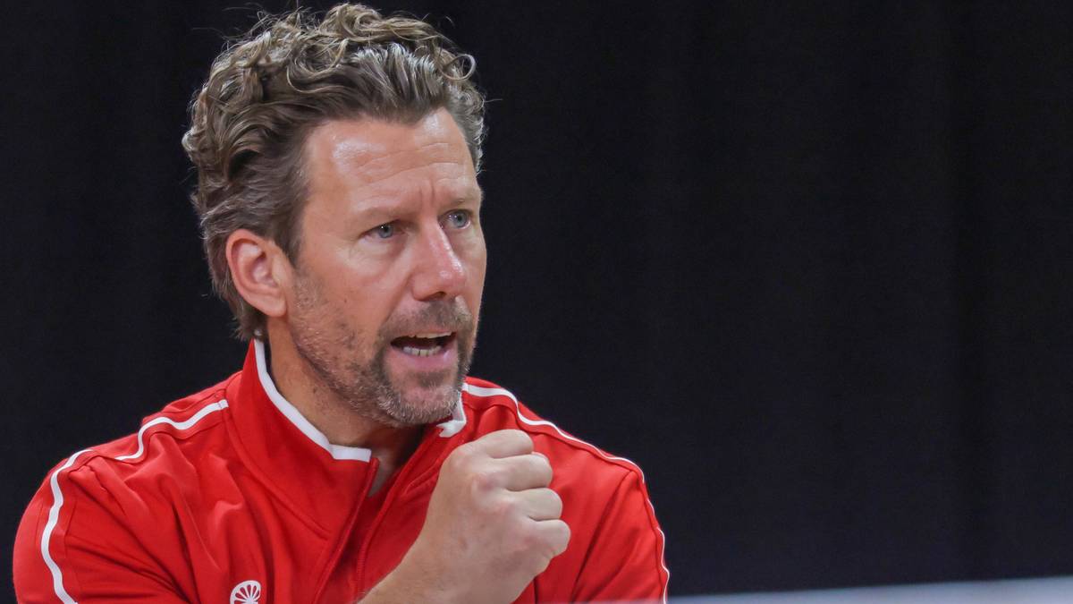 Portret Wima Fissette'a, trenera w czerwonej bluzie sportowej, z zaciśniętą pięścią i otwartymi ustami.