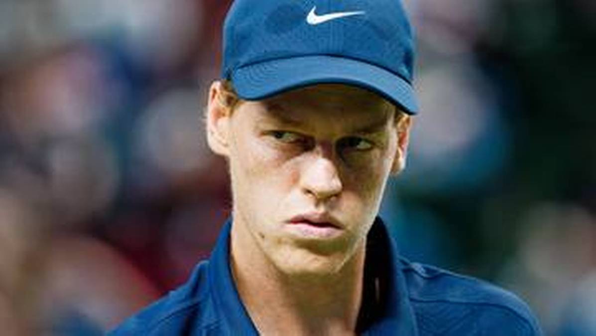 Portret Jannika Sinnera w niebieskiej czapce z daszkiem, patrzącego z zamyśloną miną w bok.