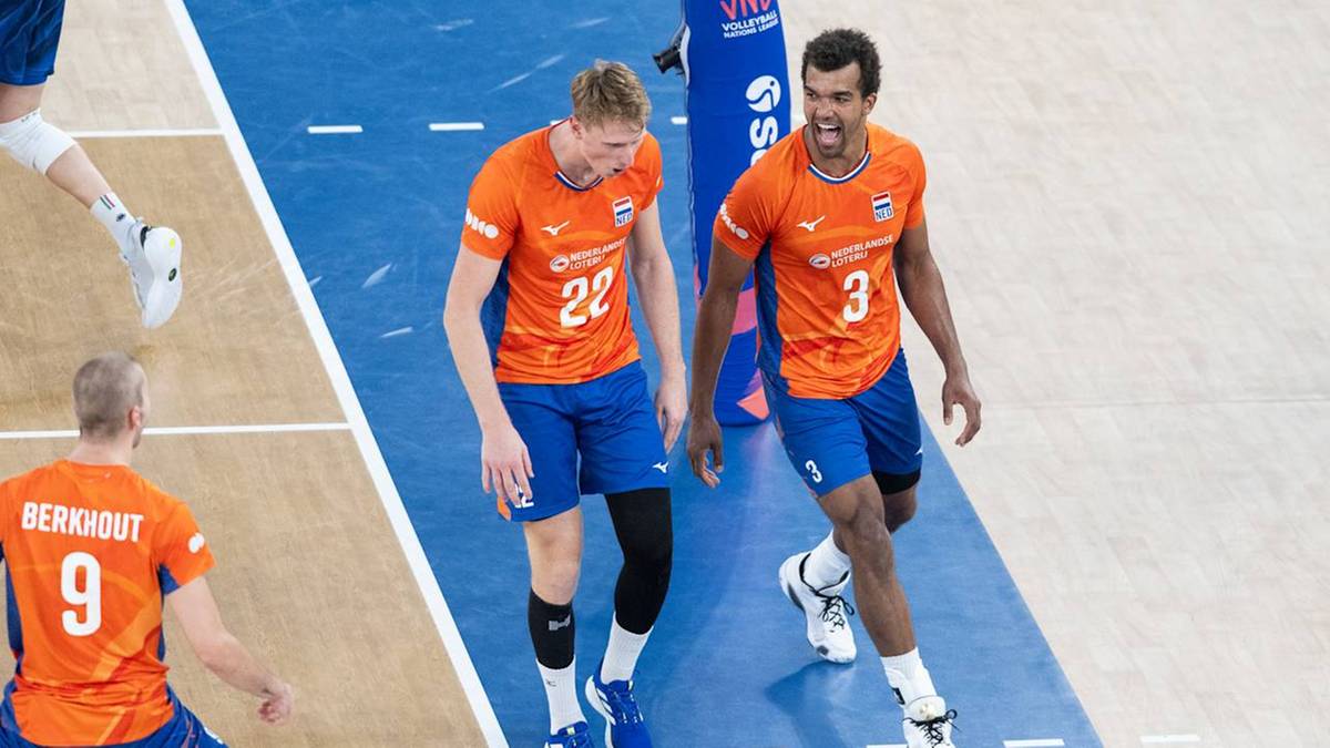 Dwóch siatkarzy w pomarańczowych koszulkach i niebieskich spodenkach idzie po boisku, rozmawiając.