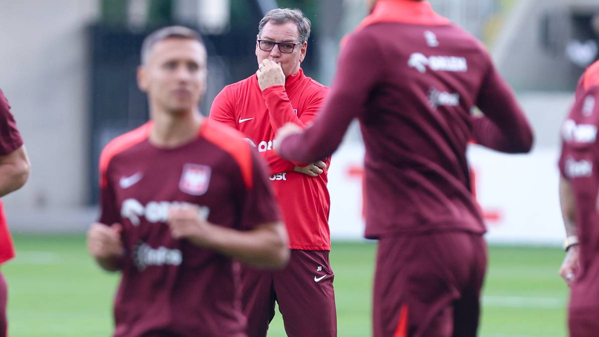 Trener piłki nożnej w czerwonej bluzie obserwuje trening swoich zawodników.