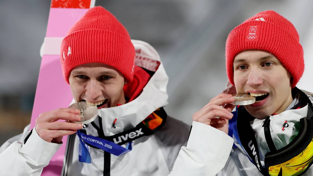 Dw&oacute;ch polskich skoczk&oacute;w narciarskich w czerwonych czapkach prezentuje swoje medale, uśmiechając się do kamery.