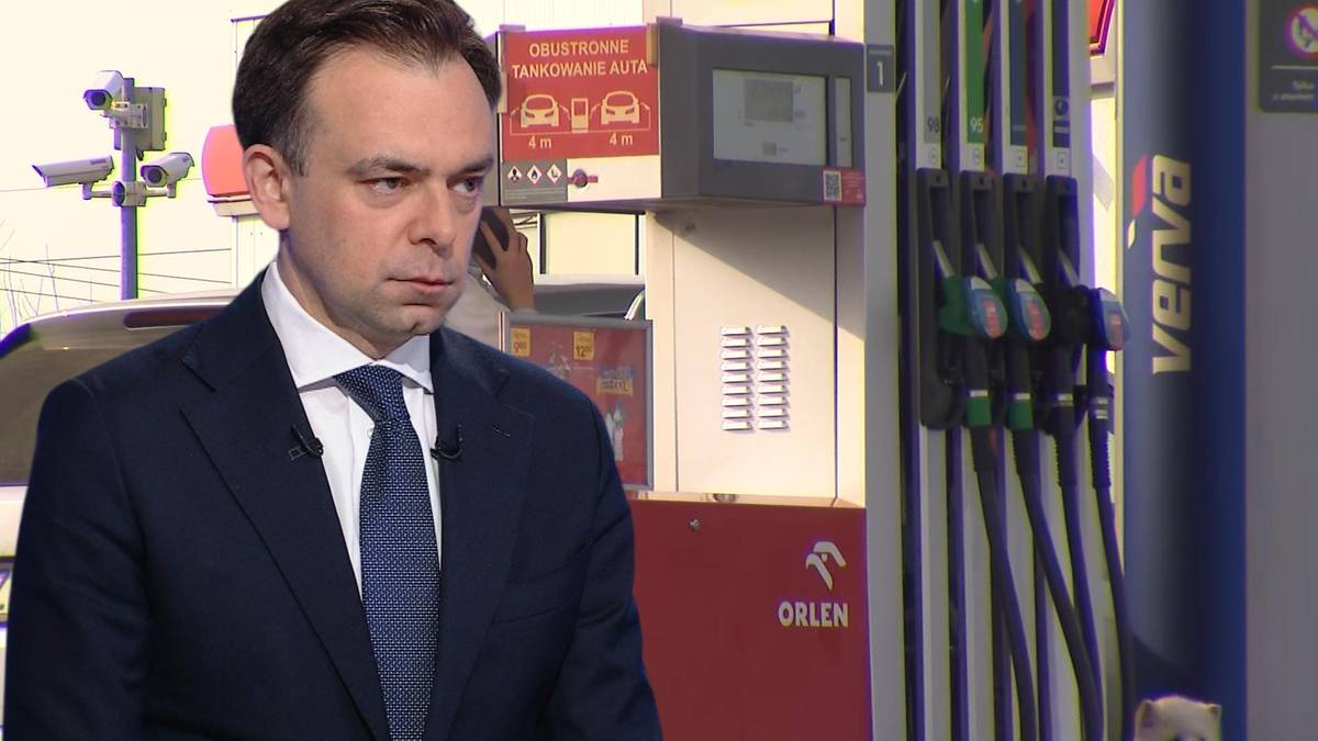 Mężczyzna w garniturze przed dystrybutorami paliwa na stacji benzynowej.