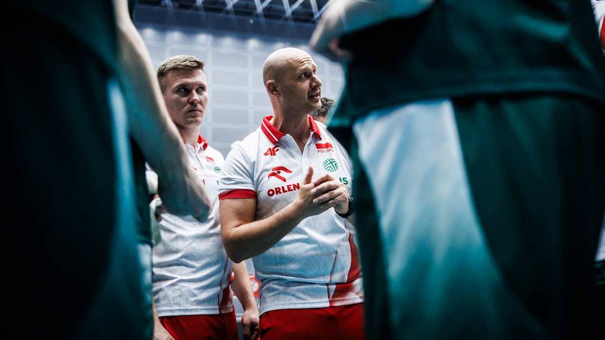 Siatkarze w strojach sportowych, jeden z nich, trener, przemawia, gestykulując rękami.