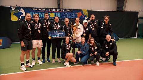 Grupa uśmiechniętych sportowc&oacute;w w strojach sportowych pozuje do zdjęcia z pucharem i medalem.