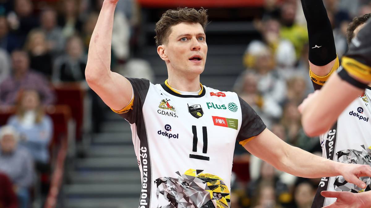 Siatkarz w białej koszulce z czarnymi elementami, z numerem "11" na piersi, unosi prawą rękę.