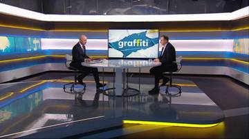 Dw&oacute;ch mężczyzn w garniturach siedzi naprzeciwko siebie przy okrągłym stole w studiu telewizyjnym.