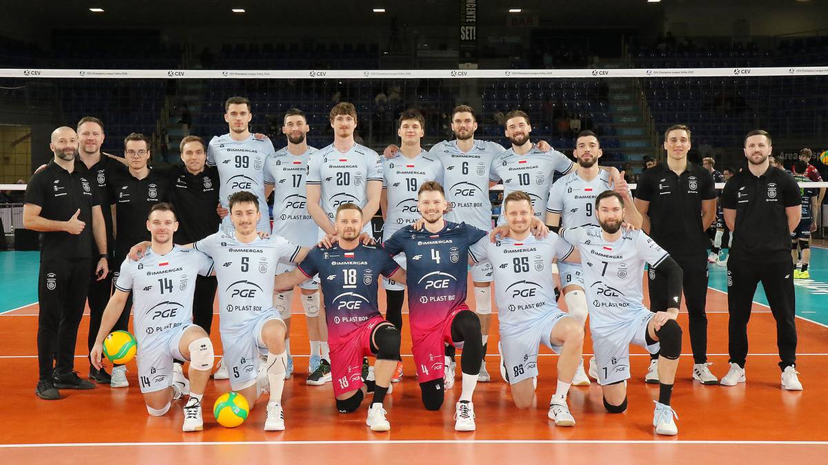 Drużyna siatkarska w komplecie pozuje do zdjęcia na boisku.