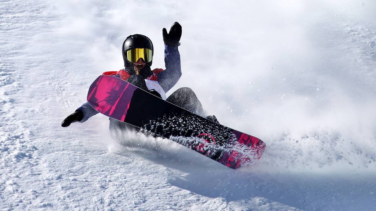 Snowboardzistka na stoku, uniesiona ręka, chmura śniegu