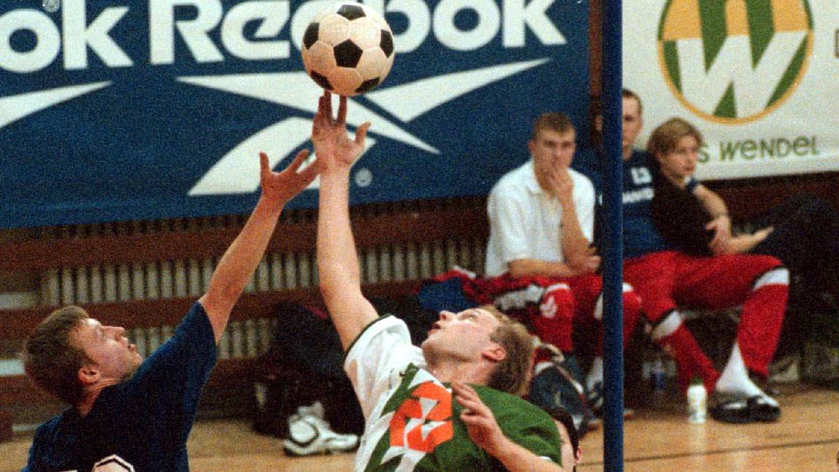 Dwóch zawodników w akcji podczas meczu korfballu, próbujących złapać piłkę zawieszoną nad głowami.