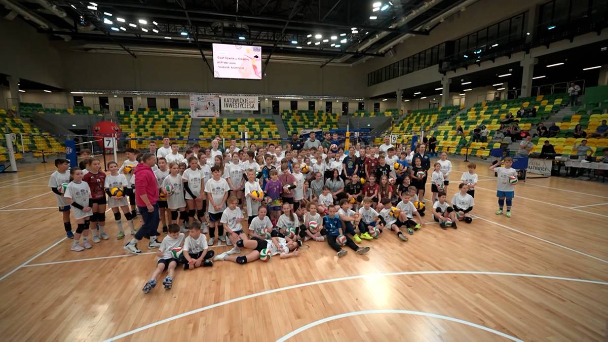 Grupa dzieci i dorosłych w białych koszulkach na boisku sportowym.