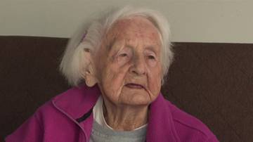 Portret starszej kobiety z siwymi włosami, ubranej w r&oacute;żową bluzę.