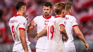 Piłkarze reprezentacji Polski w białych strojach rozmawiają na boisku.