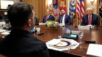 Mężczyźni siedzą przy stole konferencyjnym w sali z flagami, dyskutując o planie pokojowym.