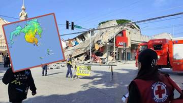 Grupa ratownik&oacute;w w kamizelkach z czerwonym krzyżem na tle zniszczonego budynku po trzęsieniu ziemi na Filipinach.