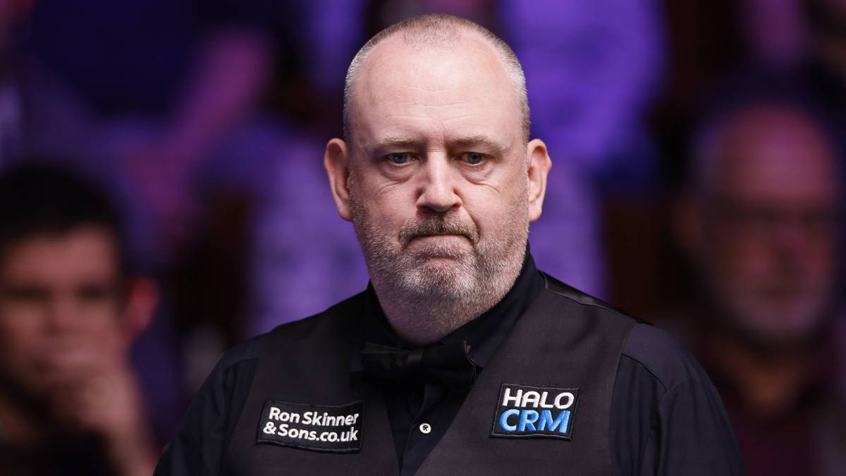 Snookerzysta w czarnej kamizelce z napisem "HALO CRM" i "Ryana Skinnera", trzymający kij snookerowy.