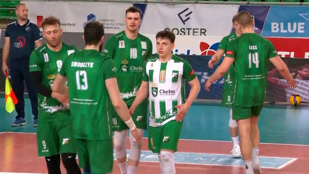 Grupa siatkarzy w zielonych strojach podczas meczu, skupiona na rozmowie na boisku.