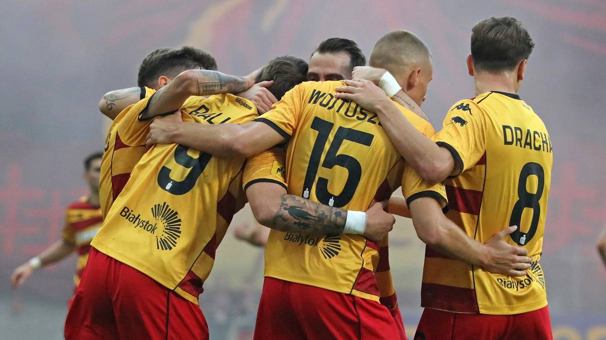 Piłkarze Jagiellonii Białystok świętujący zdobycie bramki, obejmując się i ściskając.