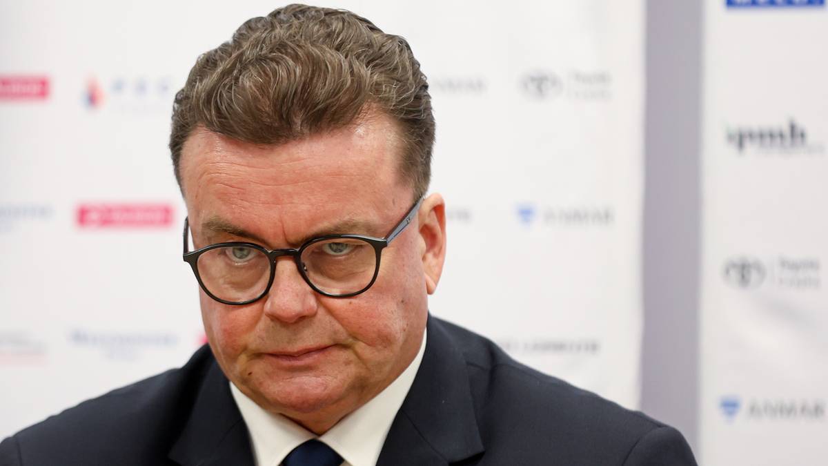 Portret mężczyzny w garniturze i okularach, patrzącego w obiektyw.