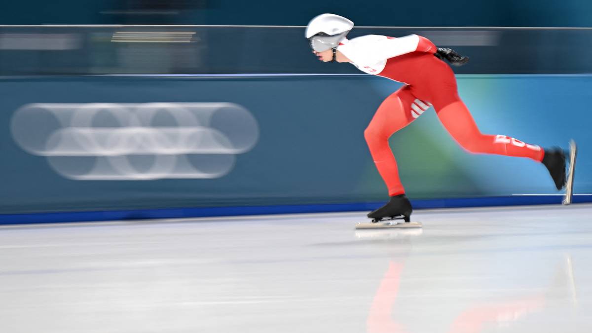 Panczenista w biało-czerwonym stroju ślizgający się po lodowym torze z rozmytym tłem