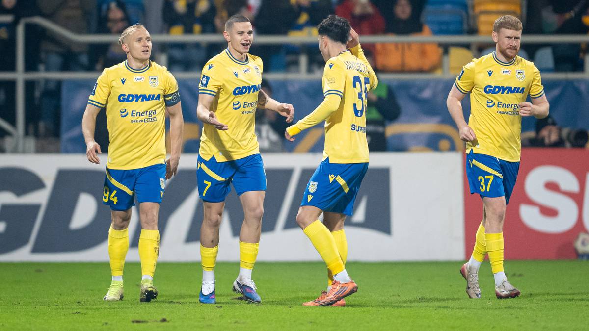 Pięciu piłkarzy w ż&oacute;łtych koszulkach z niebieskimi elementami stoi na boisku piłkarskim.