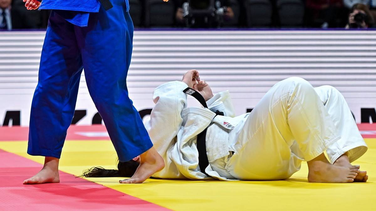 Dwóch zawodników judo na macie, jeden leży na plecach, drugi stoi obok.