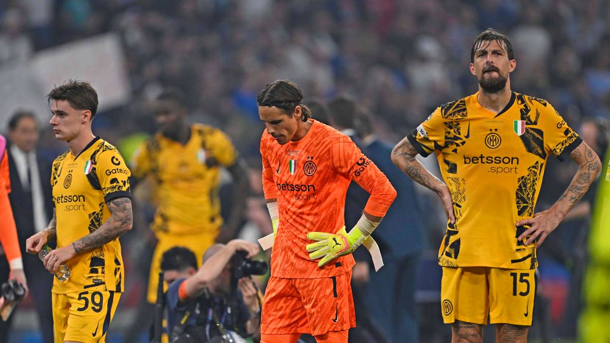 Trzech piłkarzy w żółtych strojach stoi na boisku piłkarskim, jeden z nich w pomarańczowym stroju bramkarza.