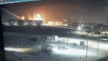 Nocny widok eksplozji i pożaru w mieście z zabudowaniami mieszkalnymi w tle.