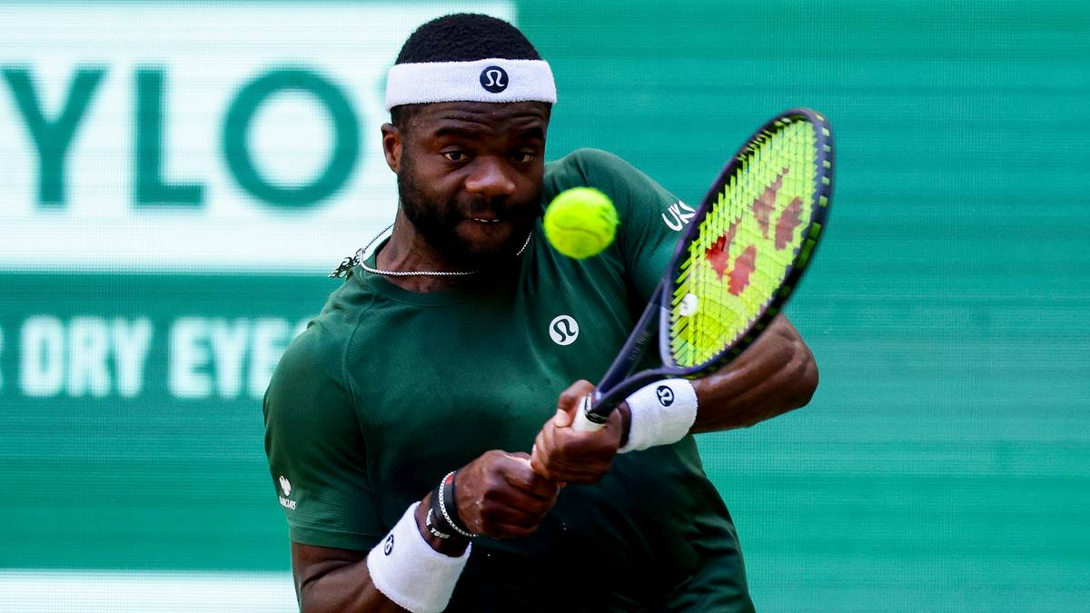 Tenisista Frances Tiafoe w akcji, uderzający piłkę rakietą podczas meczu.
