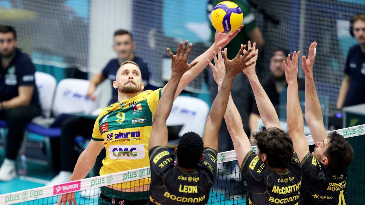 Gracz w żółto-zielonym stroju z numerem 9 podbija piłkę do siatkówki, podczas gdy czterech graczy przeciwnych drużyn w czarnych strojach próbuje go zablokować.