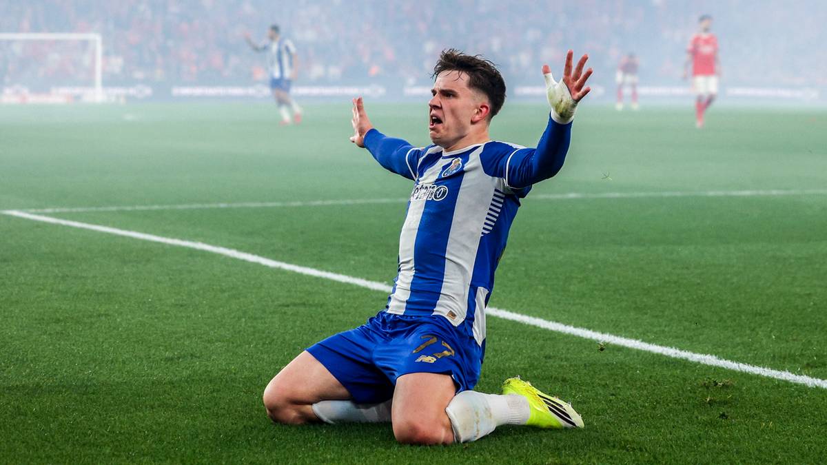 Piłkarz w niebiesko-białym stroju klęczy na boisku z uniesionymi rękami, celebrując bramkę.