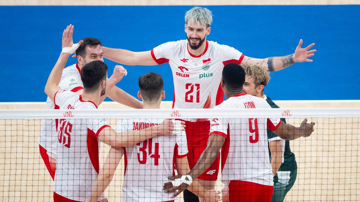 Siatkarze reprezentacji Polski w białych strojach z czerwonymi elementami, świętujący zwycięstwo na siatce.