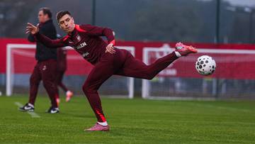 Piłkarz w bordowym stroju kopie piłkę na boisku treningowym.