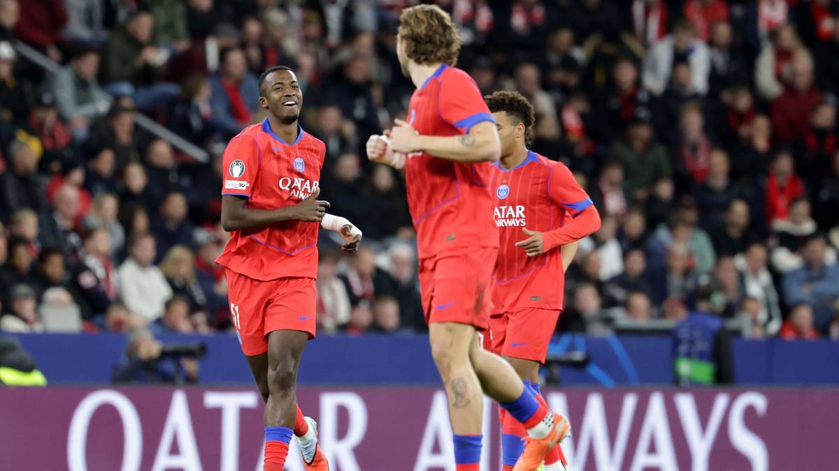 Piłkarze w czerwonych strojach biegają po boisku w stronę trybun, z których widać tłum kibiców. Na pierwszym planie widoczni są trzej gracze z numerami na koszulkach, uśmiechnięci i wyraźnie zadowoleni. Za nimi, na tle zielonej murawy, znajduje się baner z napisem "QATAR AIRWAYS".