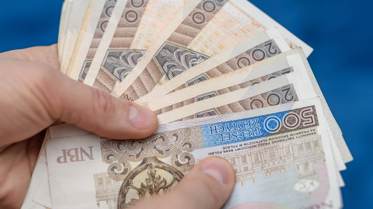 Dłoń trzymająca plik polskich banknotów o nominałach 200 i 500 złotych.