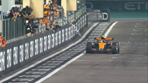 Samoch&oacute;d Formuły 1 zespołu McLaren w pomarańczowo-niebieskich barwach jedzie po torze wyścigowym podczas nocnego wyścigu, z trybunami pełnymi widz&oacute;w w tle.