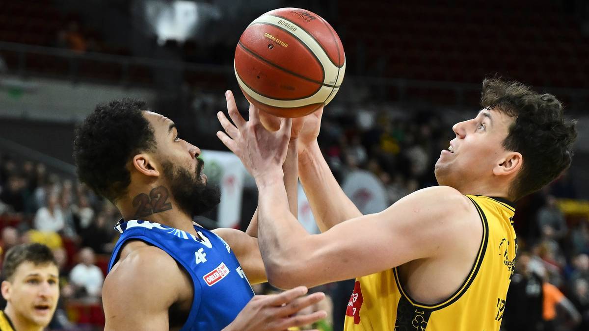 Dw&oacute;ch koszykarzy rywalizuje o piłkę podczas meczu, jeden w ż&oacute;łtej, drugi w niebieskiej koszulce.