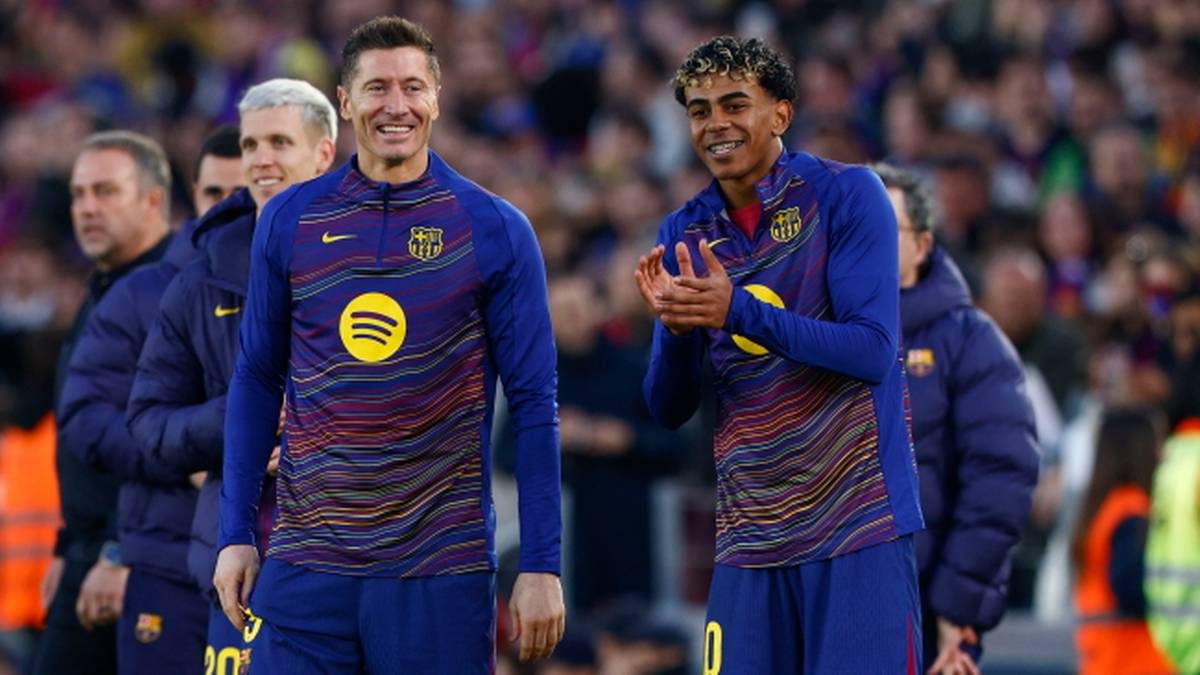 Piłkarz Robert Lewandowski w niebieskiej koszulce z ż&oacute;łtymi i purpurowymi pasami, z opaską kapitana na lewym ramieniu, uśmiecha się do kamery.