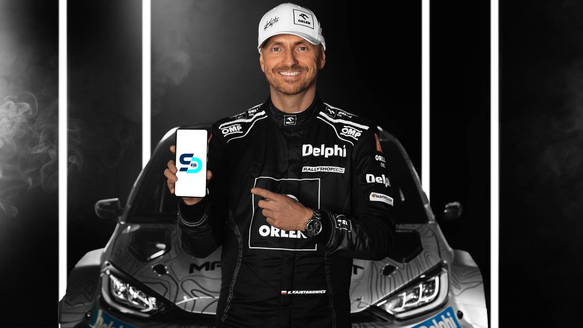 Kajetan Kajetanowicz, kierowca rajdowy, prezentuje smartfon z aplikacją FIA Smart Driving Challenge.
