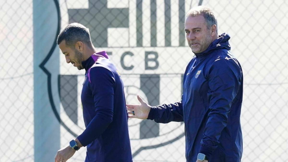 Dw&oacute;ch mężczyzn w strojach sportowych, jeden z nich jest trenerem, na tle logo FC Barcelona.