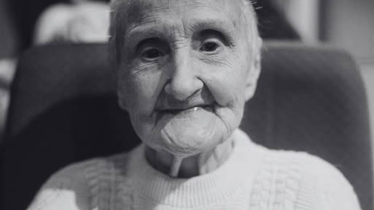 Portret Anny Kurek, uczestniczki Powstania Warszawskiego, kobiety w podeszłym wieku, ubranej w jasny sweter, z przypiętym do piersi medalem.